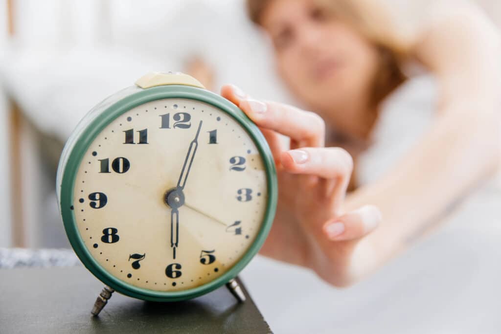 Person reaching to stop vintage alarm clock in morning light.