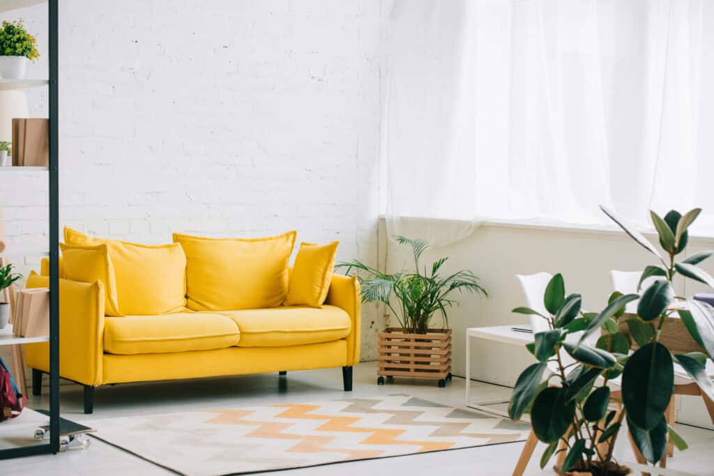 Depositphotos_265407896_XL Modern living room with a vibrant yellow sofa, green plants, and natural light from large windows. | Sky Rye Design Modern living room with a vibrant yellow sofa, green plants, and natural light from large windows.