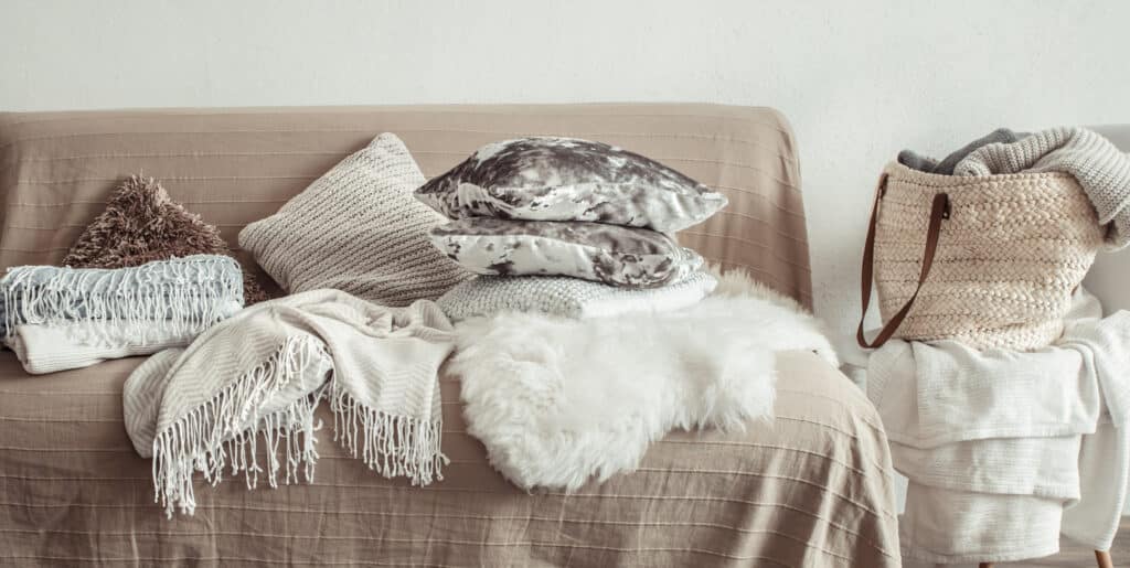 Cozy living room with neutral pillows, throw blankets, and a woven basket, perfect for a serene, stylish home décor.