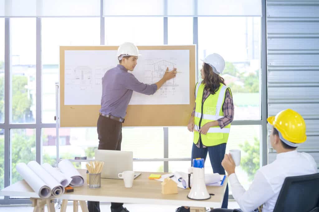 Architects in hard hats discussing building plans at construction site meeting.