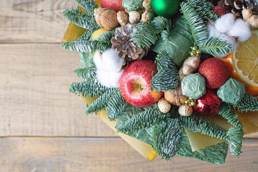 Festive holiday arrangement with pine branches, apples, nuts, and ornaments on a wooden surface.