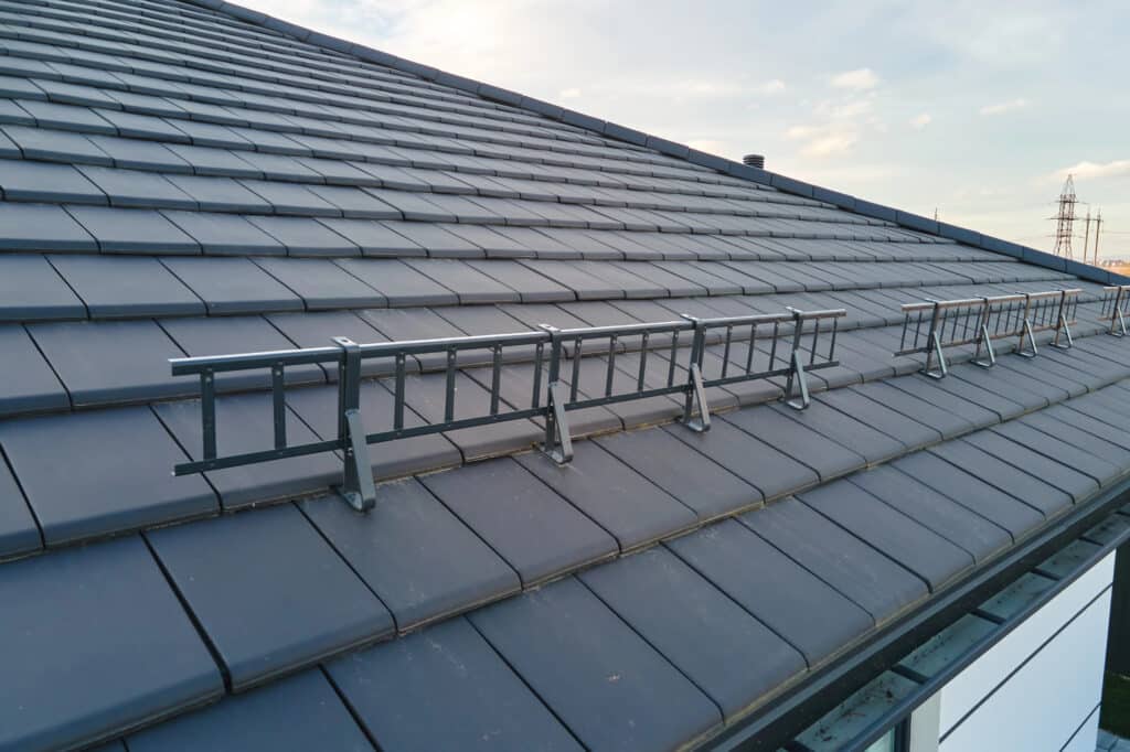 Modern rooftop with black tiles and snow guard ladder under clear sky.