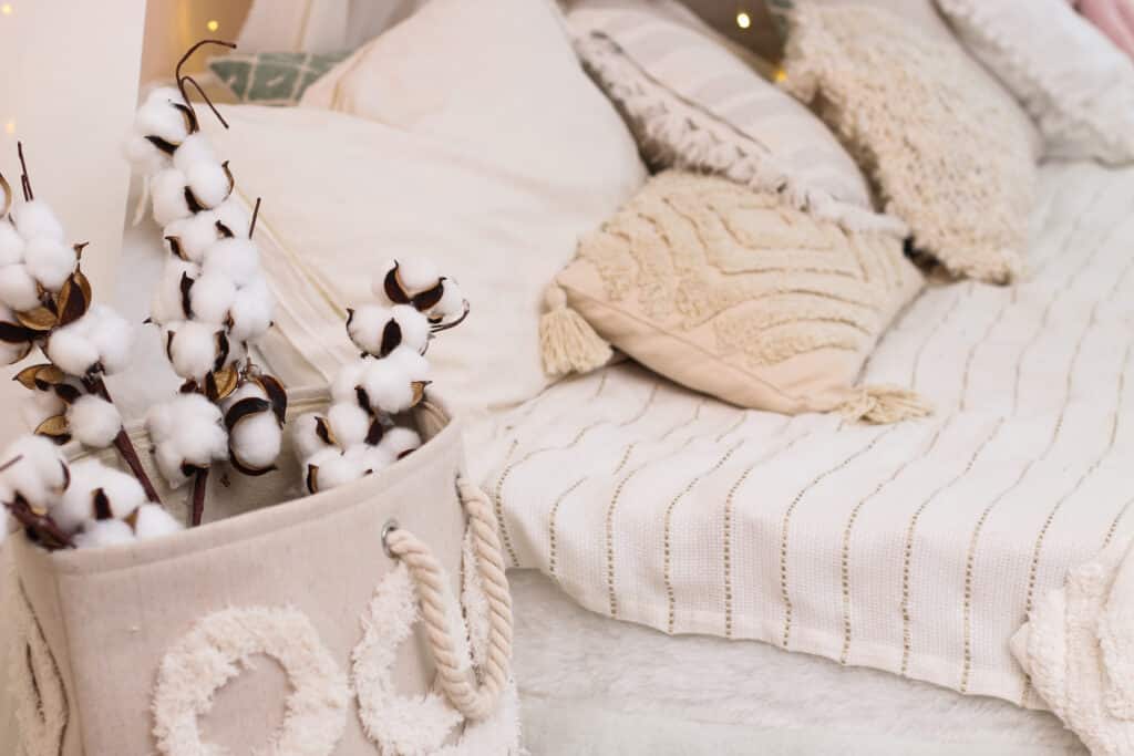 Sprigs of cotton stand in a vase as a decoration of the interior and decor Cozy neutral bedroom with cotton decor in a basket, textured pillows, and a striped blanket for a serene vibe. | Sky Rye Design Cozy neutral bedroom with cotton decor in a basket, textured pillows, and a striped blanket for a serene vibe.