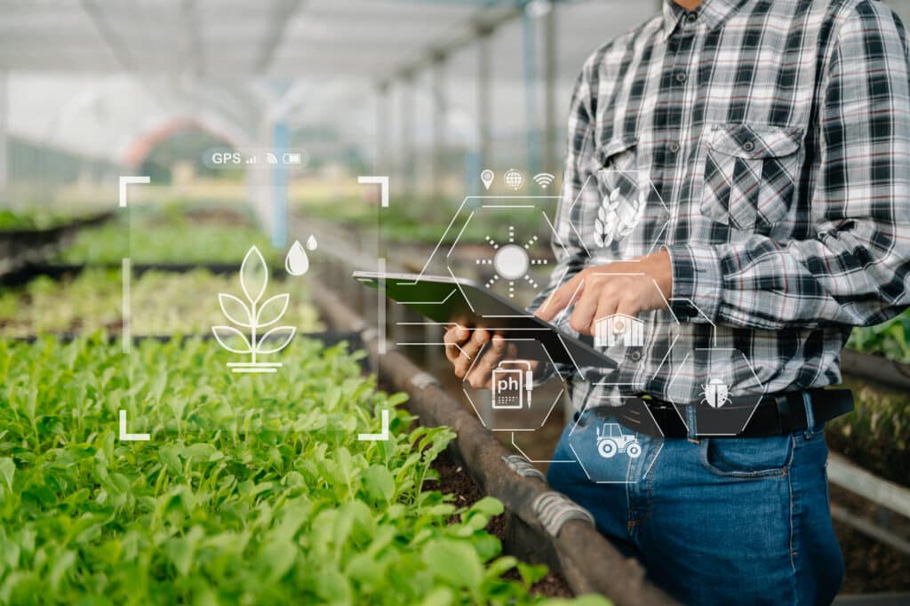 Person using tablet for smart farming in greenhouse with digital agriculture icons overlay.
