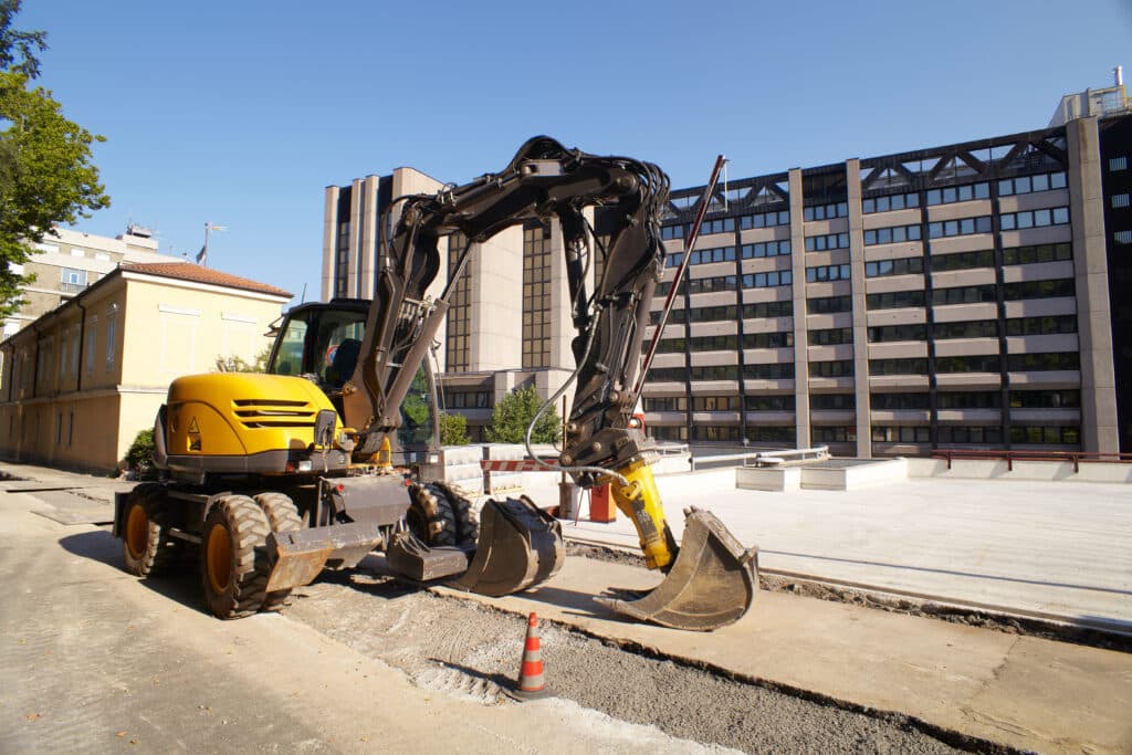 Yellow construction vehicle on a city street, with buildings and blue sky in the background.