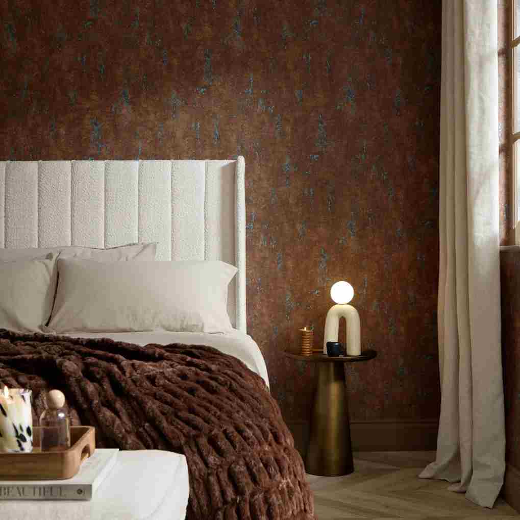 Cozy bedroom with plush bed, dark brown blanket, elegant side table, and warm lighting.