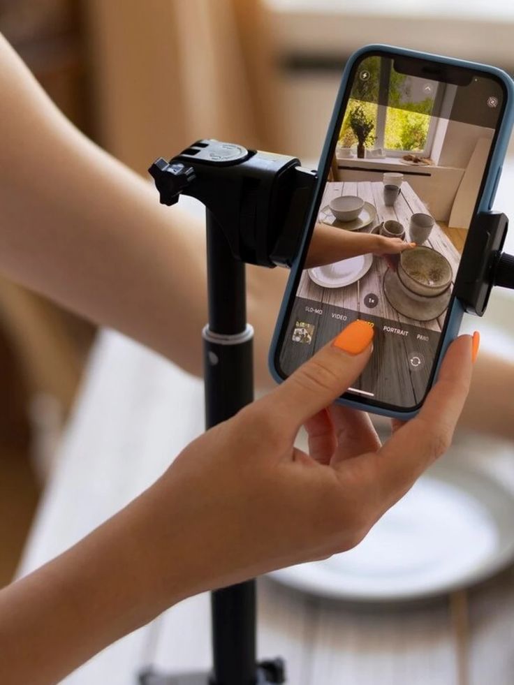 Smartphone filming a prepared dining table setup with dishes and cups for social media content creation.