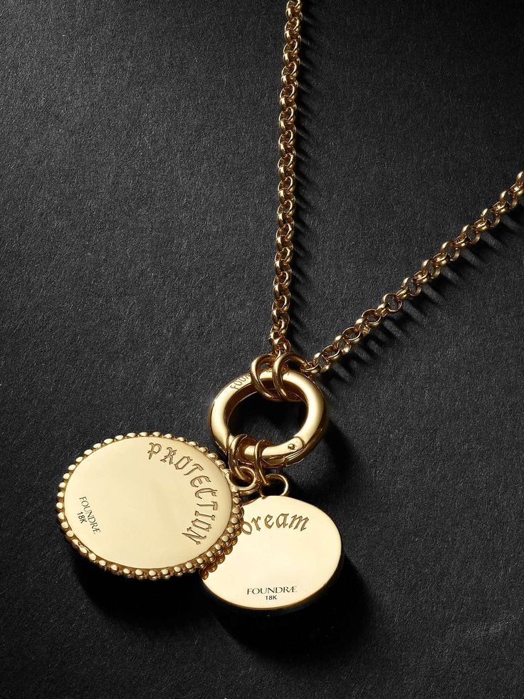 Gold necklace with two engraved pendants reading Protection and Dream on a dark background.