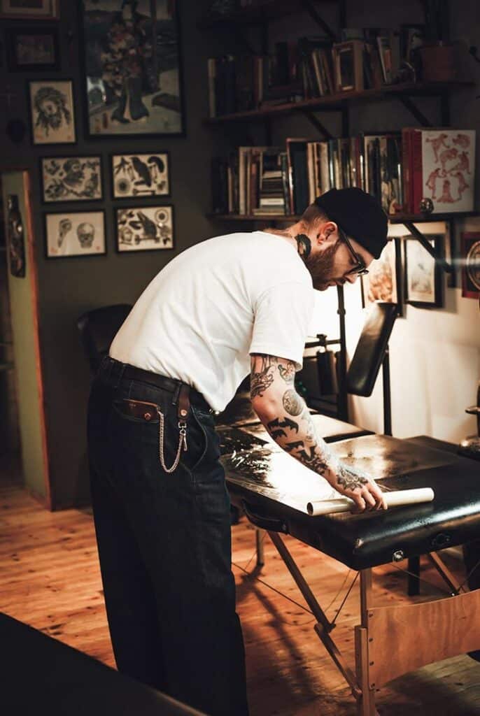 Tattoo artist preparing workspace in studio with wall art and books.