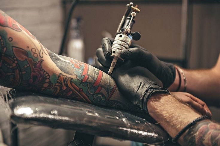 Tattoo artist creating colorful arm design with tattoo machine in studio.