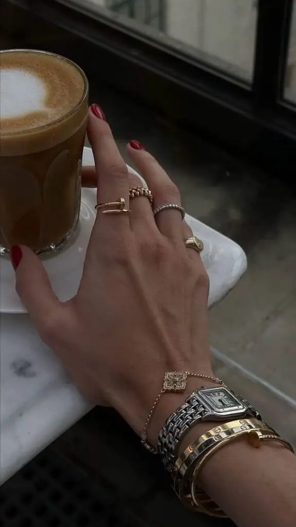 Elegant hand with jewelry holding a coffee cup on a marble table, showcasing stylish bracelets and rings.
