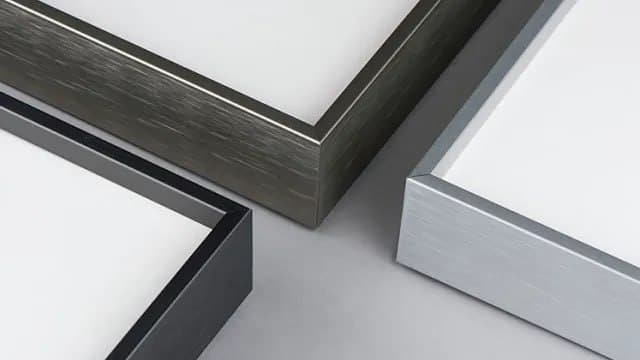 Three metallic frame corners in black, bronze, and silver on a gray surface, showcasing texture and modern design.