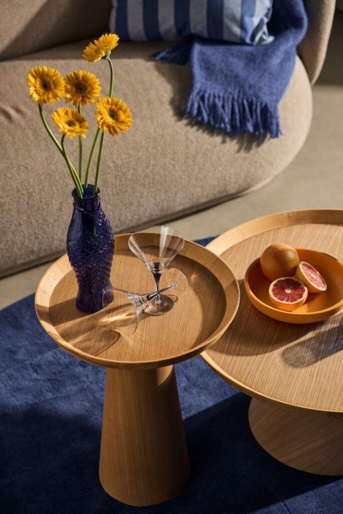 Stylish living room setup with wooden tables, a blue vase with flowers, martini glasses, and a plate of grapefruit.