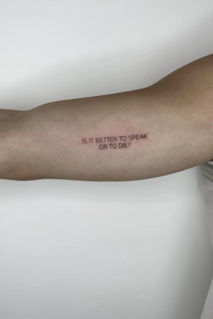 Arm tattoo reads Is it better to speak or to die? against a plain white background.