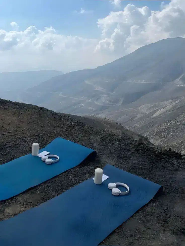 Two blue yoga mats with candles set on a mountain top, overlooking scenic cloudy hills in the background.