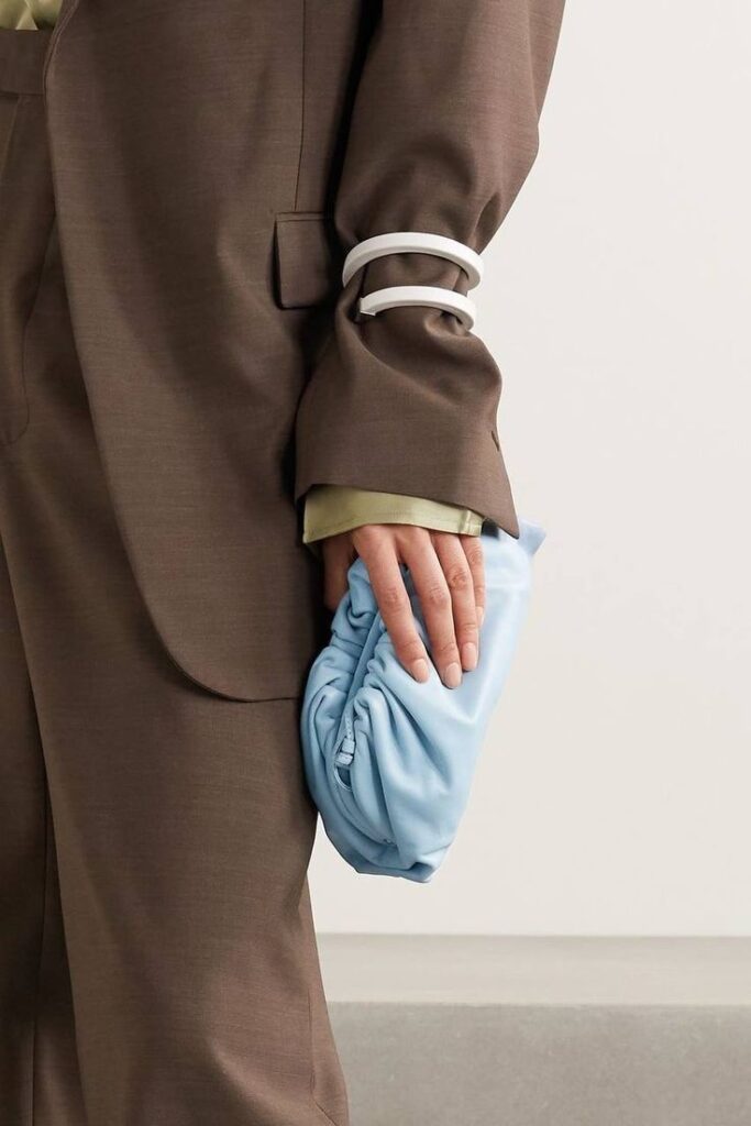 Person in brown suit holds a stylish blue clutch with white arm bracelets. Fashionable and modern accessories.