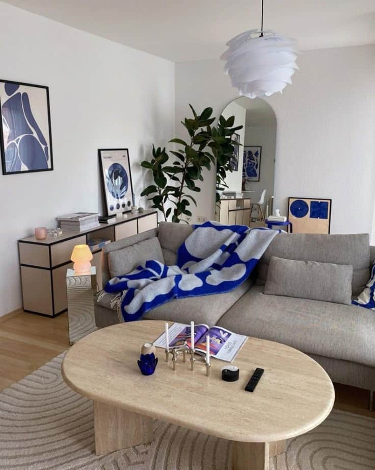 Modern living room with gray sofa, blue throw, stylish decor, and indoor plant near arched mirror. Minimalist design.