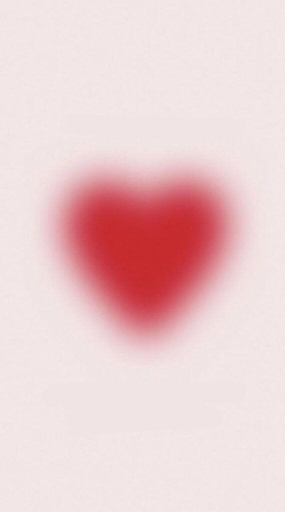 Blurry red heart shape on a soft pink background, conveying love and warmth.