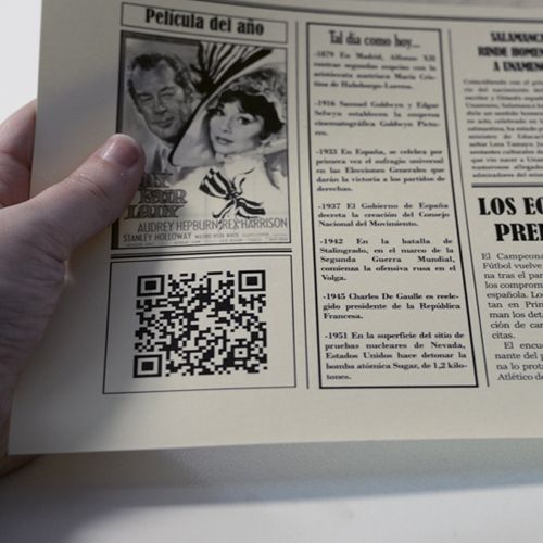 Person holding a vintage newspaper featuring an old movie poster and a QR code.