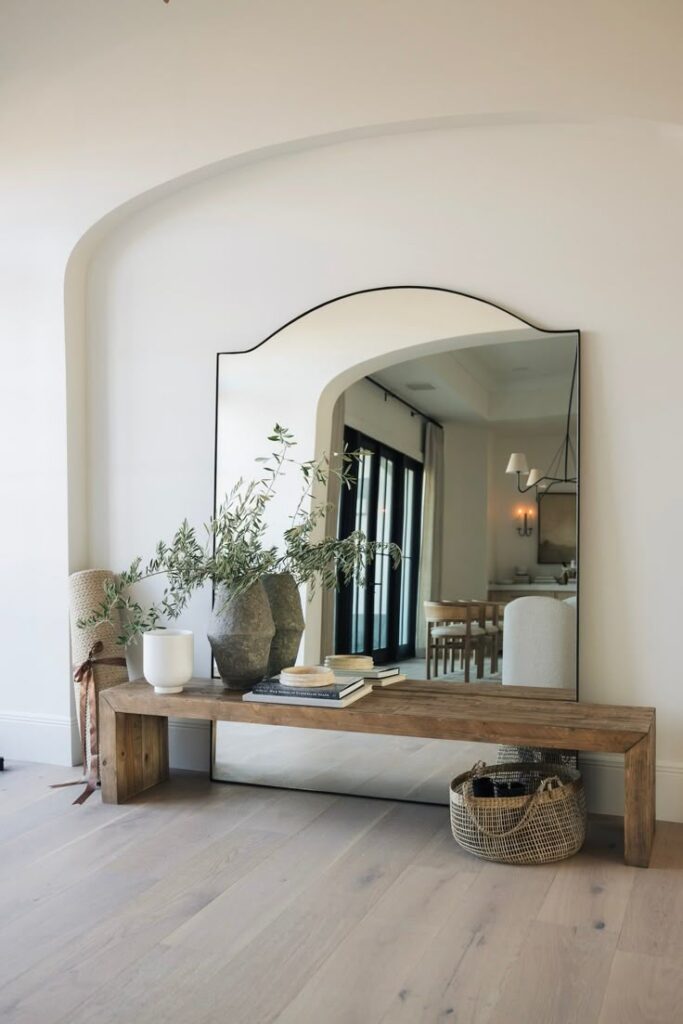 Modern hallway with large mirror, wooden bench, decorative vases, and basket, creating an elegant and minimalist aesthetic.