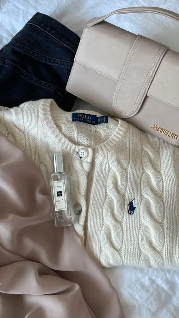 Cream cardigan with bag, perfume, pink fabric, and jeans flat lay for a chic and stylish look.