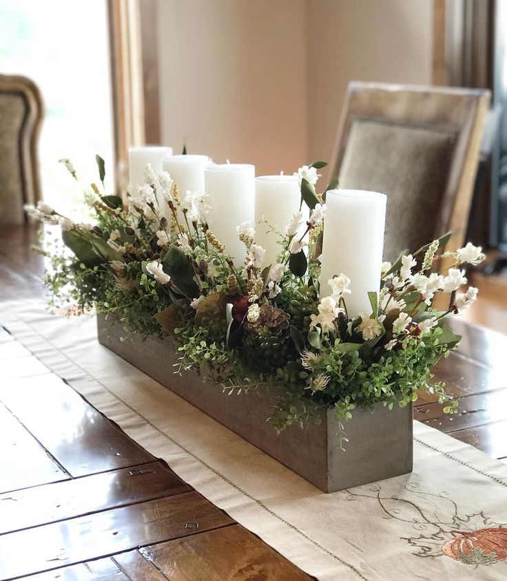 Elegant table centerpiece with white flowers and candles in a rectangular vase on a wooden dining table.