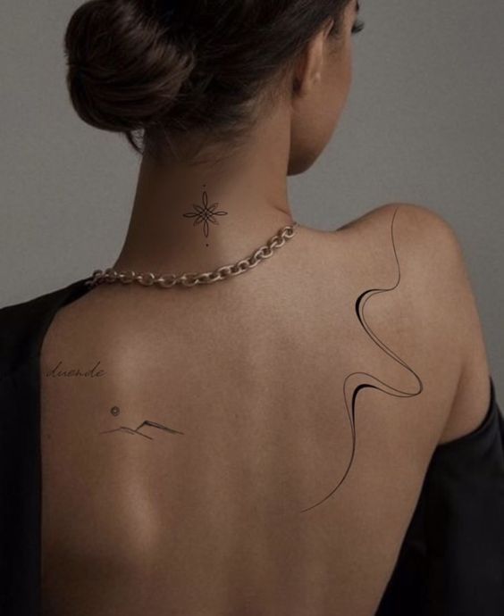 Woman with minimalist tattoos on back, wearing a chain necklace, showcasing elegant body art and style.