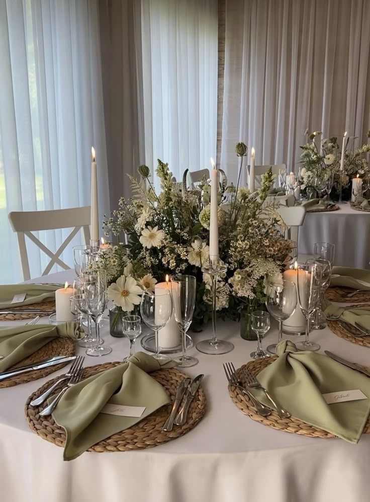 Elegant wedding table with green napkins, white floral centerpiece, and candles, creating a romantic dining setting.