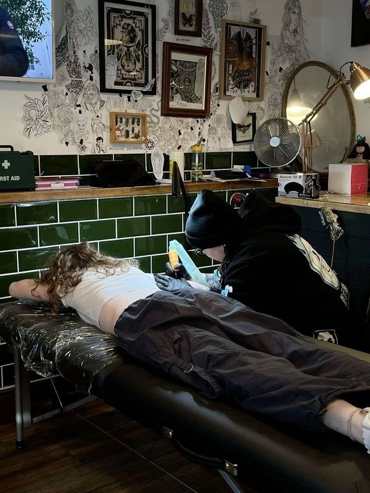 b87c24b2-faaa-4a7e-b3bb-28cc91c771e8 Tattoo artist working on client's arm in stylish studio with artwork-filled walls. | Sky Rye Design Tattoo artist working on client's arm in stylish studio with artwork-filled walls.