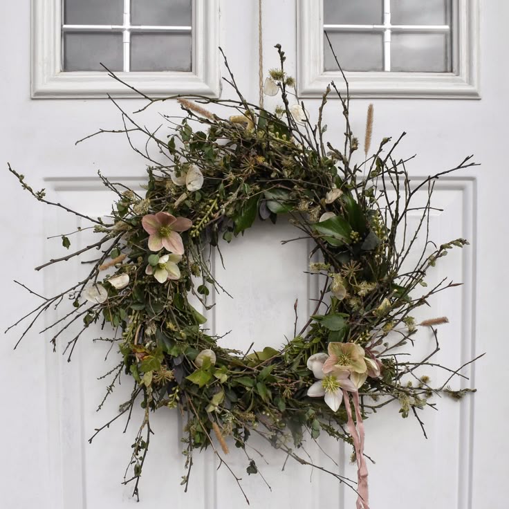 Rustic floral wreath with greenery and flowers on a white door, creating a charming natural decor accent.
