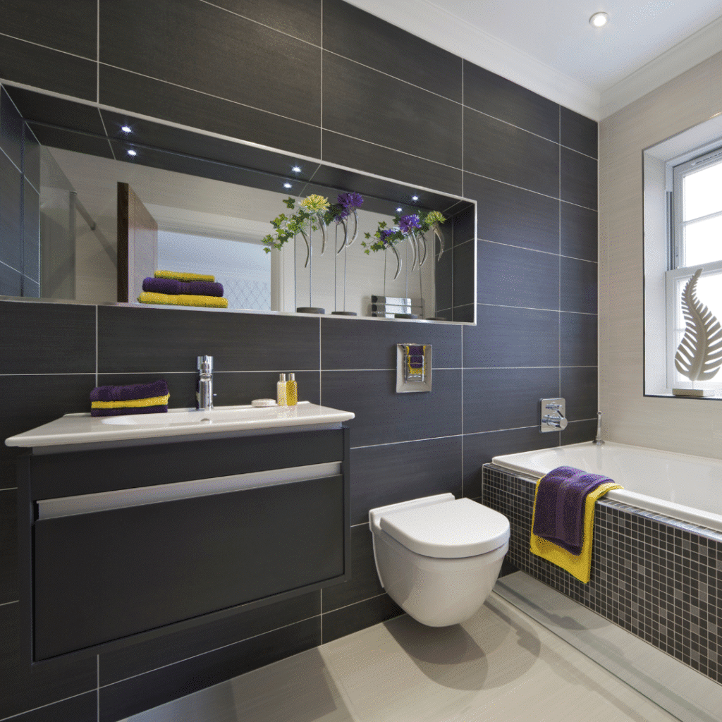 Modern bathroom with dark tiles, sleek fixtures, and vibrant towels; featuring a stylish mirror and bathtub.