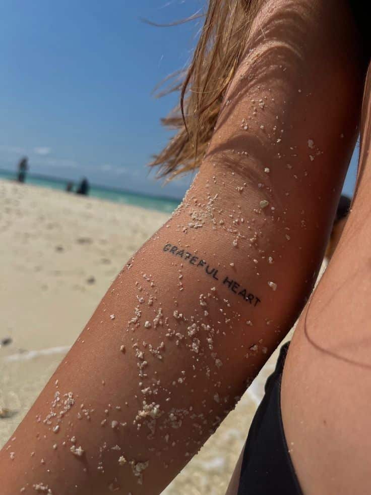 bdafa12fdc4ea6053ad6a45324831e1a Close-up of a sandy arm with Grateful Heart tattoo, beach background, clear blue sky. | Sky Rye Design Close-up of a sandy arm with Grateful Heart tattoo, beach background, clear blue sky.