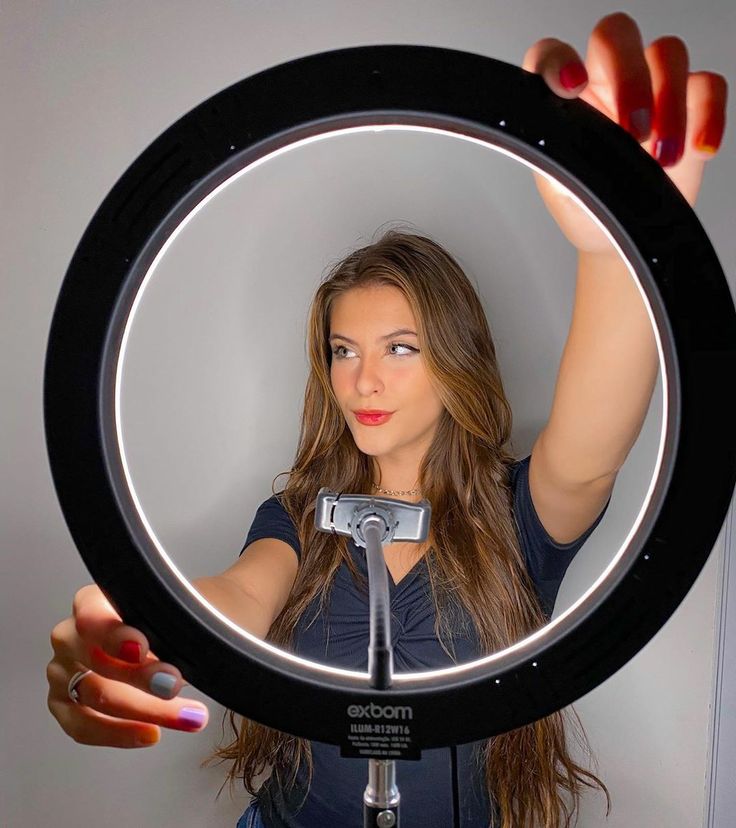 Woman adjusting LED ring light, preparing for a photo or video shoot. Illuminated face with colorful nails.