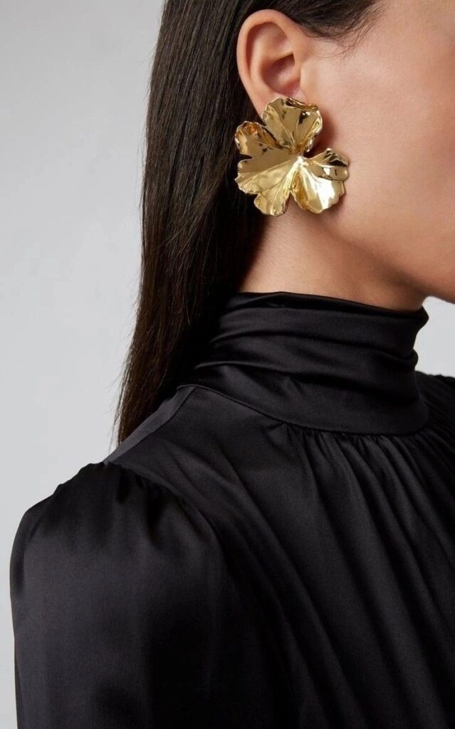 Woman wearing a black satin top with a large gold floral earring.