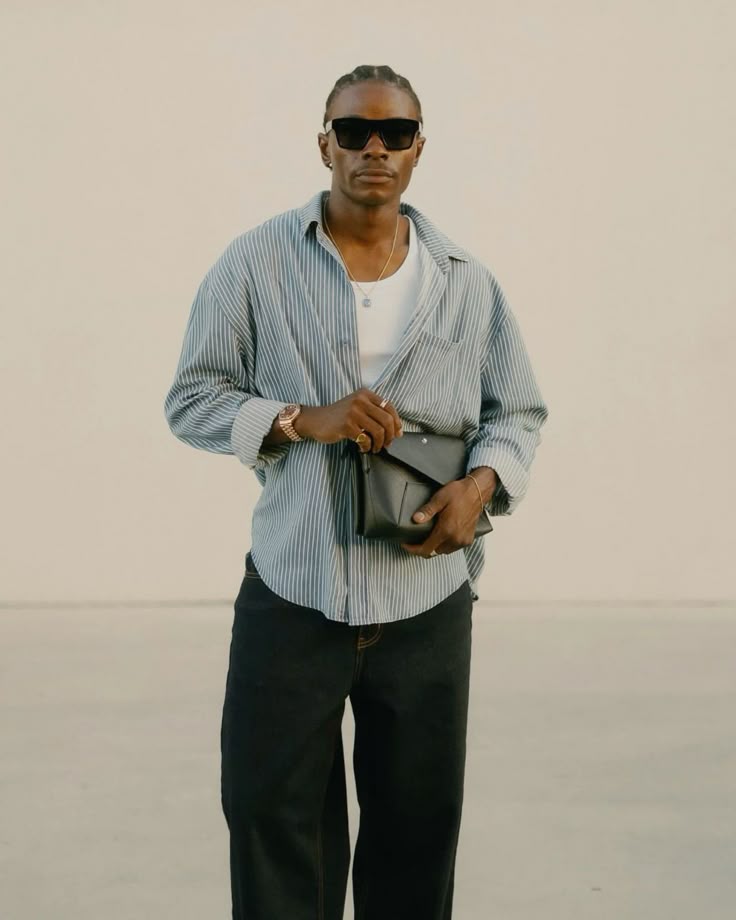 Stylish man in striped shirt and sunglasses holding a clutch outdoors.