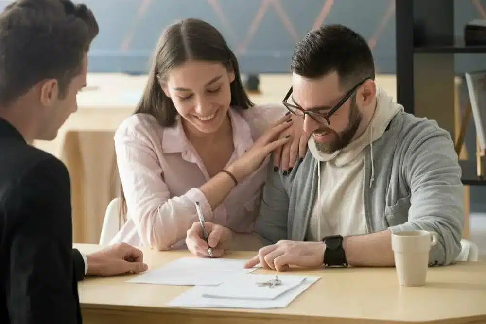 contract-close Couple happily signing documents with advisor's guidance, sitting at a table with coffee cup. | Sky Rye Design Couple happily signing documents with advisor's guidance, sitting at a table with coffee cup.