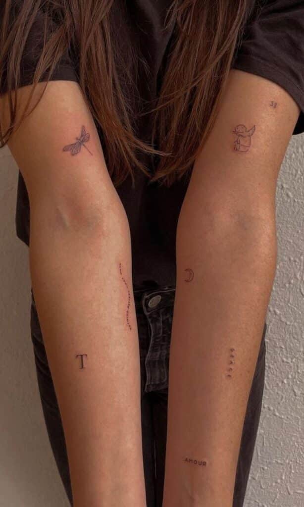 Person with minimalist tattoos on forearms, displaying dragonfly, angel, moon, and text designs on light skin.