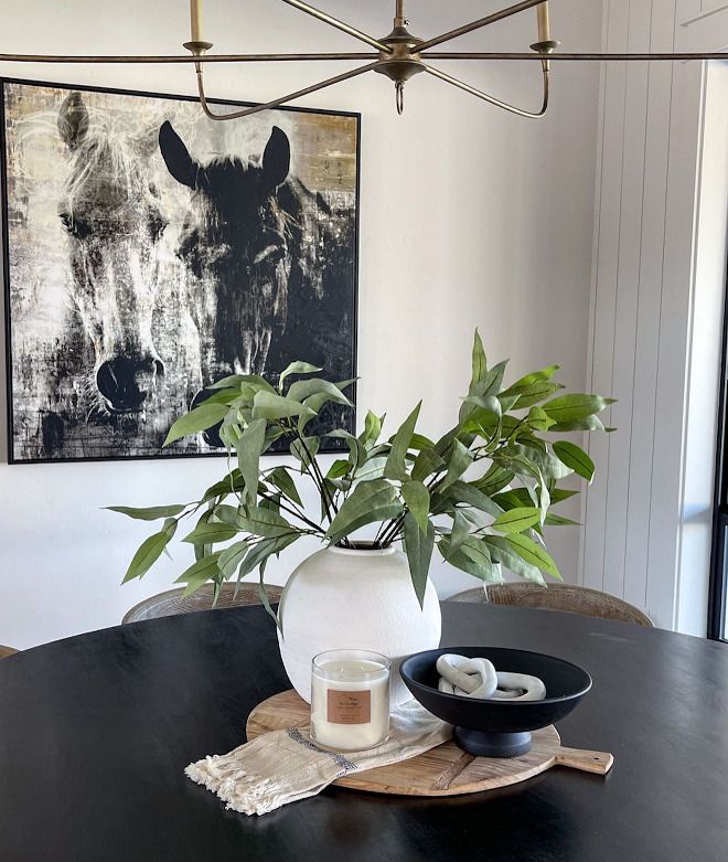 Stylish dining room decor with leafy plant, candle, and art on the wall.