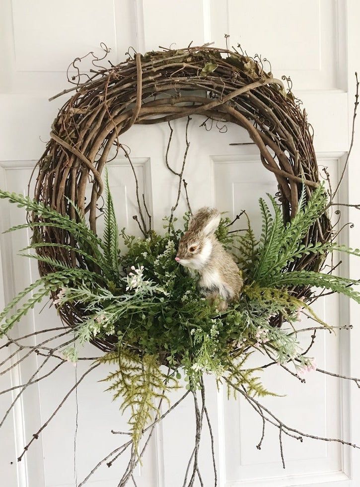 Rustic wreath with green foliage and a small decorative squirrel on a white door.