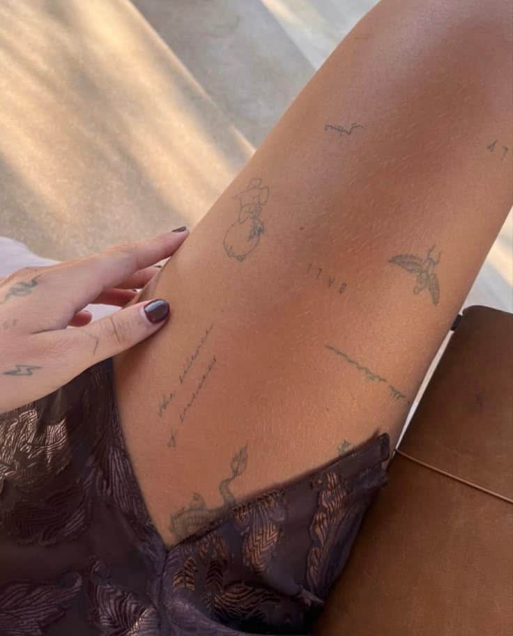 Close-up of thigh tattoos with hand resting, showcasing intricate designs and a lace garment edge.
