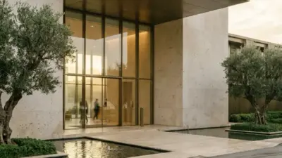 Modern luxury building entrance with large glass doors, marble facade, reflecting pools and landscaped olive trees.