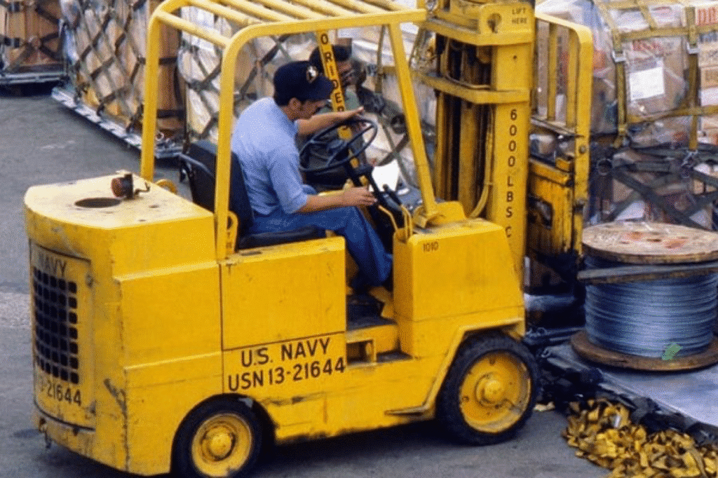 U.S. Navy personnel operating a yellow forklift, moving cargo on a military base.
