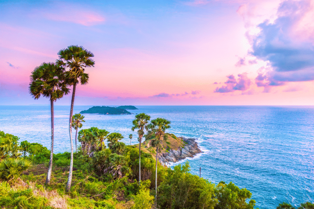 Scenic view of palm trees by the sea at sunset, vibrant pink and blue sky over lush greenery and ocean.
