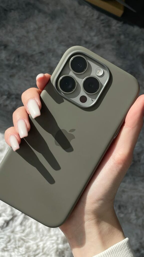 iphone 15 pro aesthetic green olive Person holding a smartphone with a gray case, showing triple camera setup in natural light. | Sky Rye Design Person holding a smartphone with a gray case, showing triple camera setup in natural light.