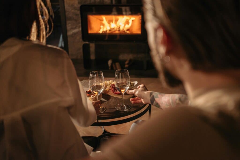 Cozy evening: Two people enjoying wine and snacks by a fireplace.
