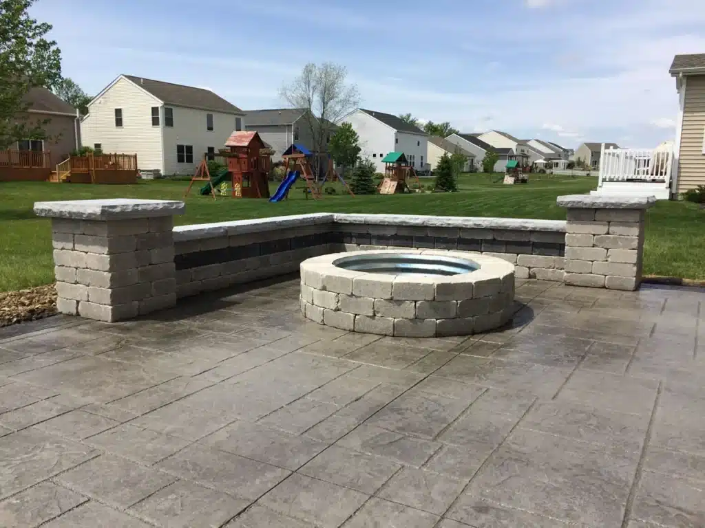 stamped-patio-with-firepit Outdoor stone patio with circular fire pit, surrounded by a neighborhood lawn with houses and playground. | Sky Rye Design Outdoor stone patio with circular fire pit, surrounded by a neighborhood lawn with houses and playground.
