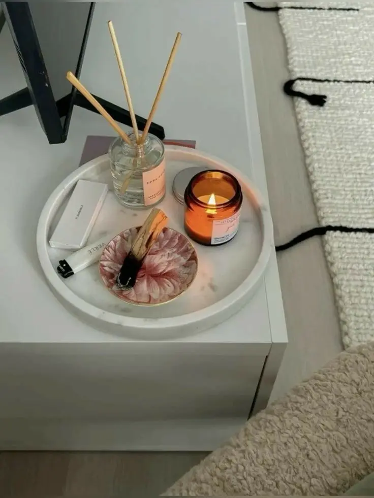 Cozy tray with lit candle, reed diffuser, and lighter on a white bedside table for a calming ambiance.