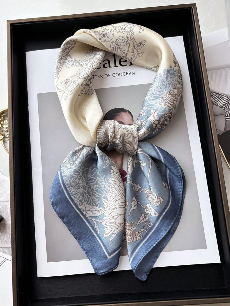 Elegant floral silk scarf in beige and blue placed on a magazine cover in a black box.