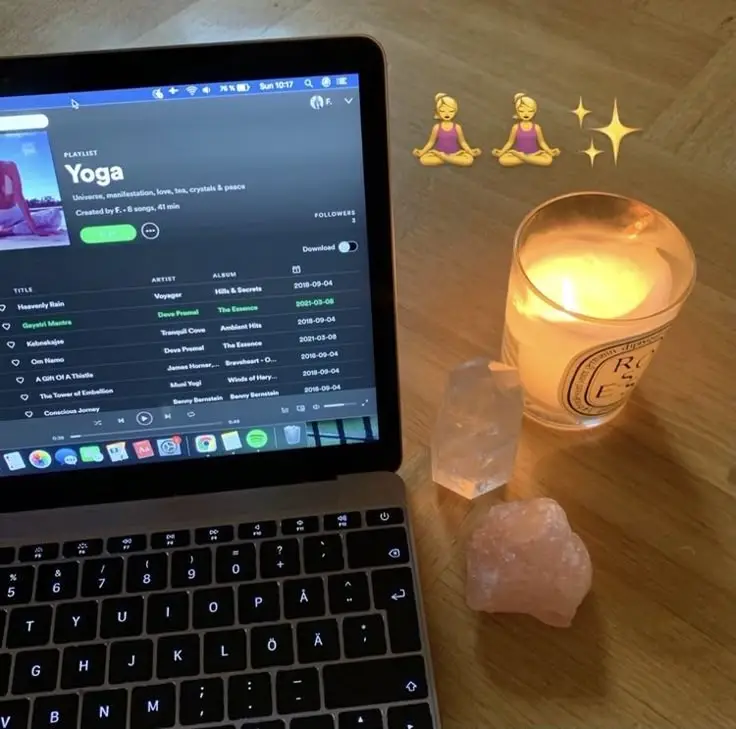 Open laptop with yoga playlist, crystals, and a lit candle on wooden table, creating a calm, peaceful atmosphere.