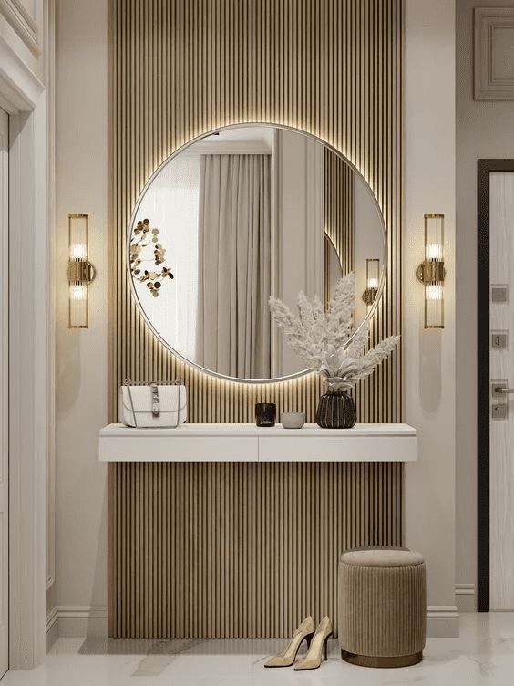 Elegant modern entryway with round mirror, wall sconces, and decor on console table, featuring neutral tones.